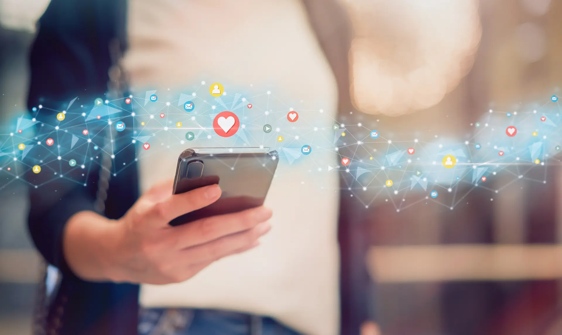 Person hält Smartphone, darüber fliegen Social-Media-Symbole wie Herz, Like, Nachricht und Netzwerk – Symbol für digitale Interaktion und Online-Kommunikation.