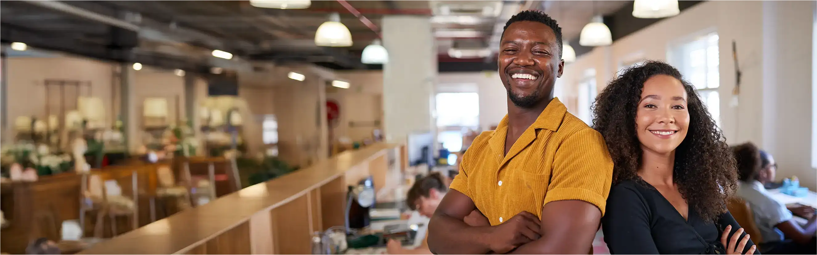 Ein Mann und eine Frau lachen gemeinsam in die Kamera und haben ihre Arme verschränkt.