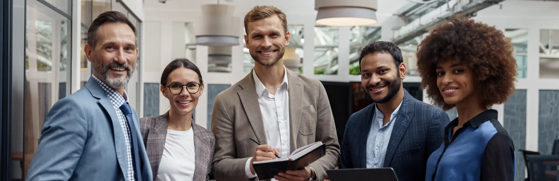 Geschäftstreffen in modernem Büro – fünf Personen im Gespräch, eine Person mit Notizbuch.