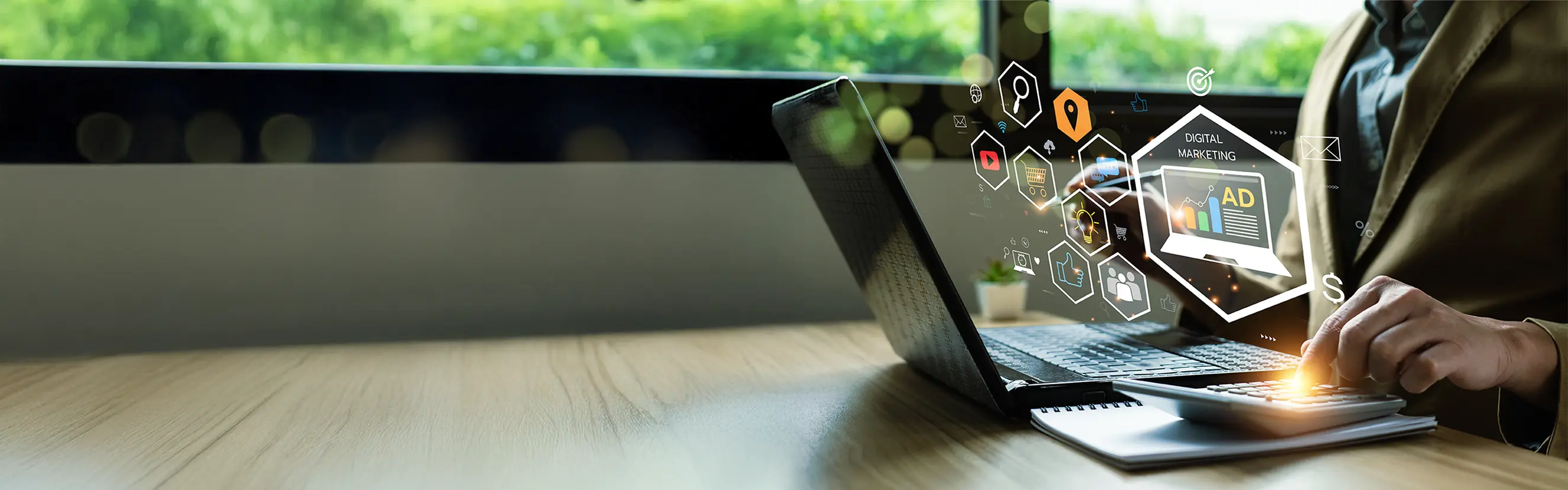 Person arbeitet am Laptop mit digitalen Icons zu Online-Marketing, Werbung und digitalen Medien, moderne Büroatmosphäre mit Fensterblick ins Grüne.