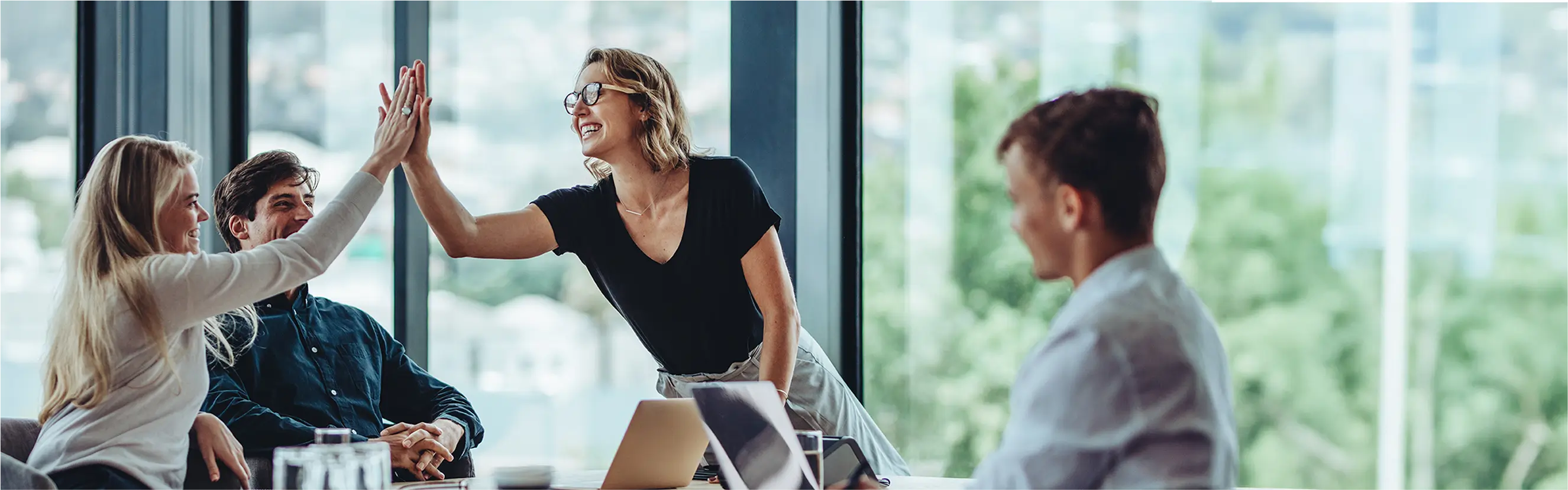 Bussiness-Situation: Vier Personen sitzen in einem Meetingraum und zwei davon klatschen sich mit den Händen gegenseitig ab.