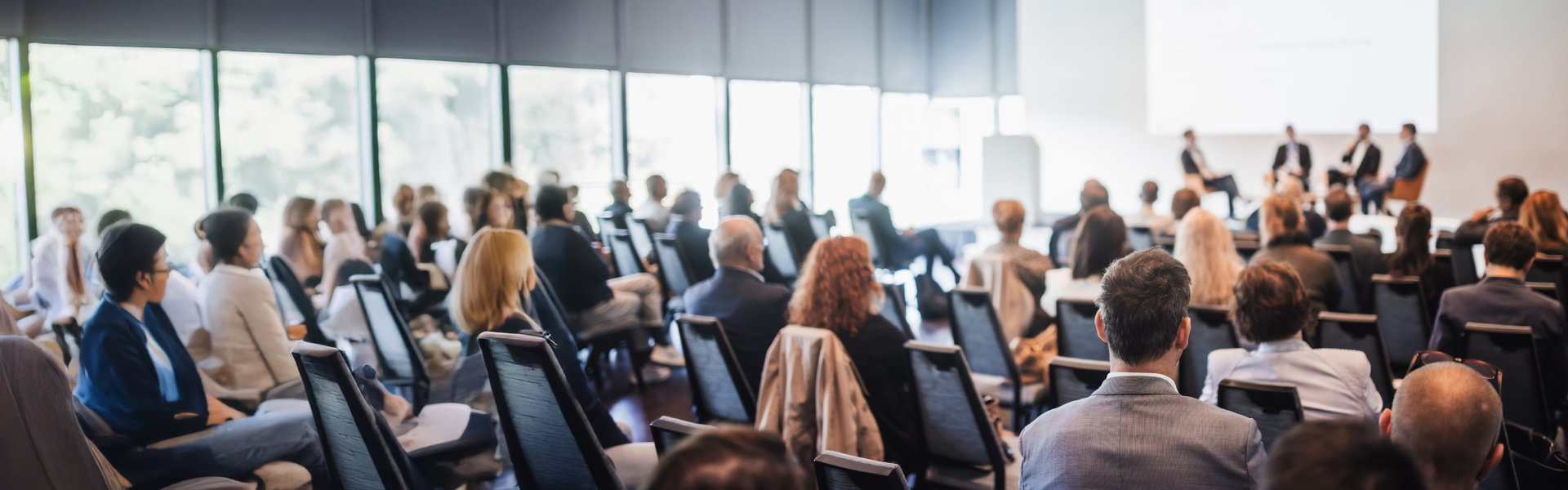 Personen sitzen in Stuhlreihen und hören vier Personen auf einer Bühne zu.