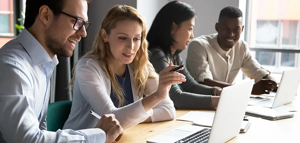 Gruppe von Mitarbeiter:innen am Arbeitsplatz vor Laptops, die miteinander kommunizieren