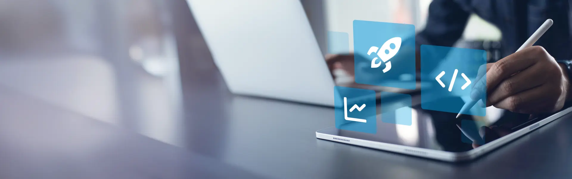 Person verwendet einen Stylus auf einem Tablet, im Hintergrund steht ein geöffneter Laptop.