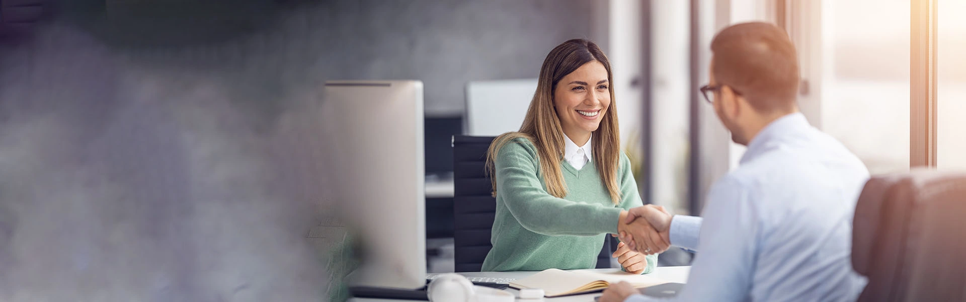 Eine Frau und ein Mann sitzen in einer Business-Situation gegenüber und schütteln sich freudig die Hände.