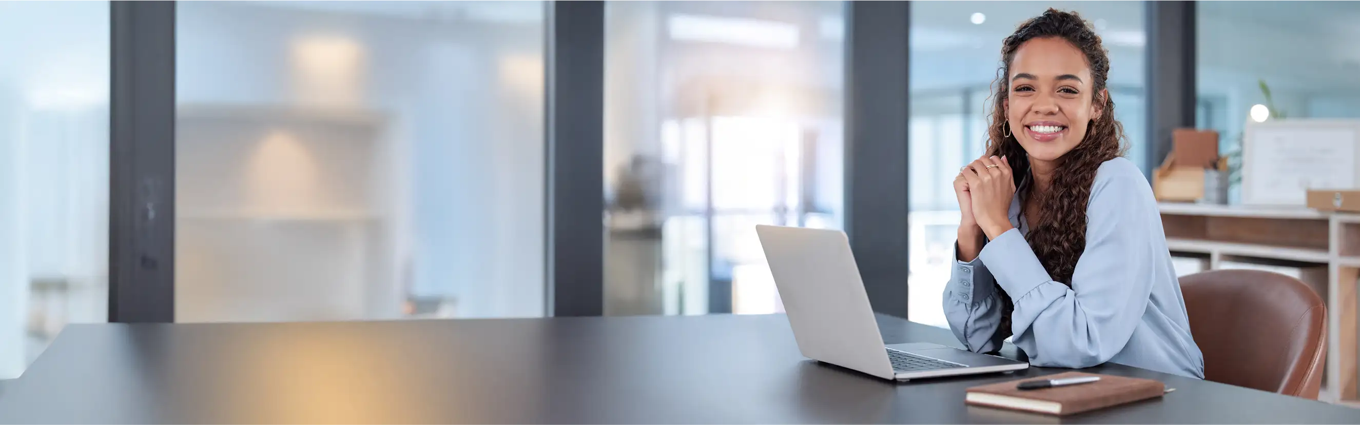 Junge Frau sitzt lächelnd vor einem Laptop und schaut in die Kamera