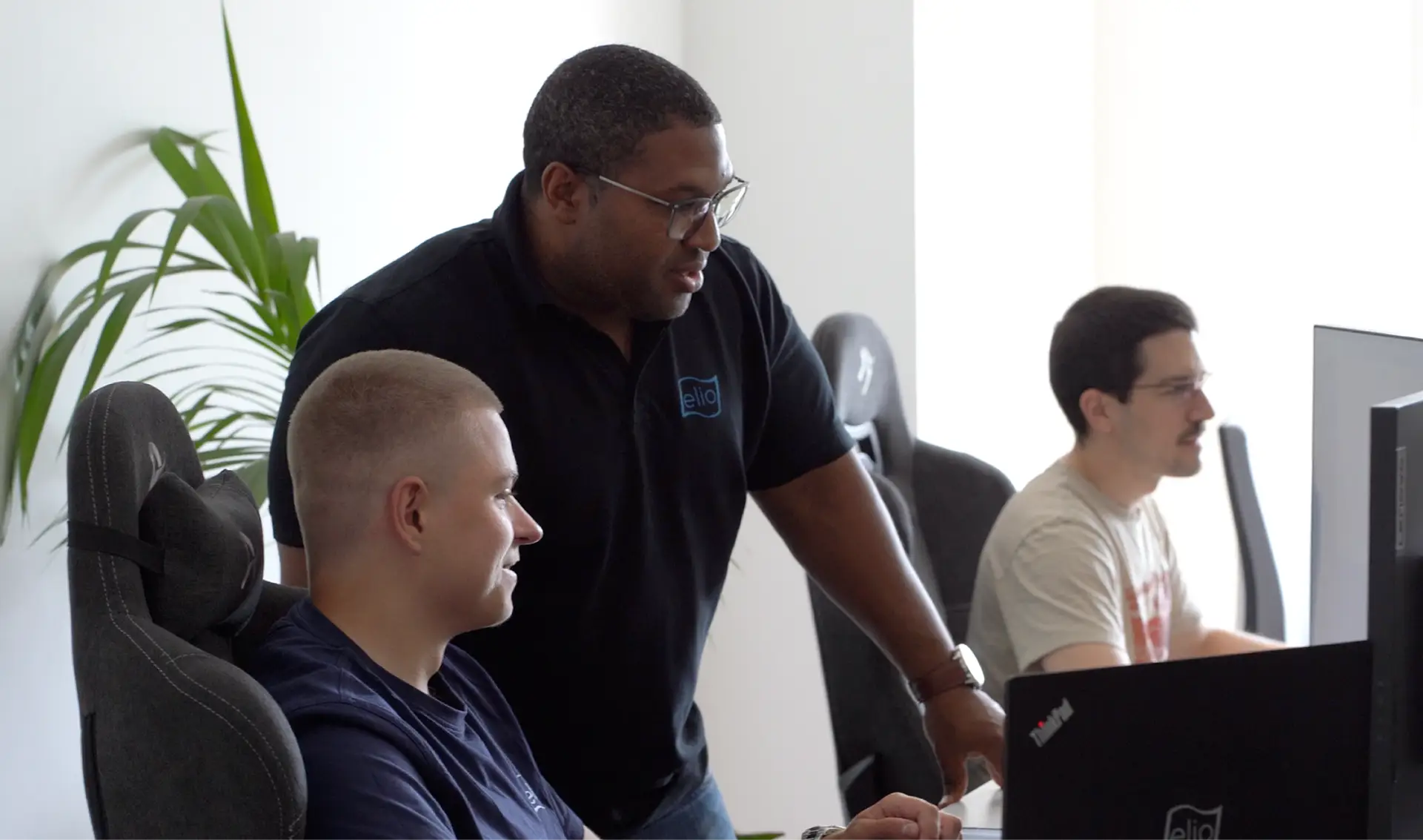 Der Mitarbeiter Albert sitzt am PC und zeigt dem Mitarbeiter Maurice etwas.